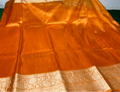 An orange Banarasi silk saree with a wide beige and gold zari border, laid out flat.
