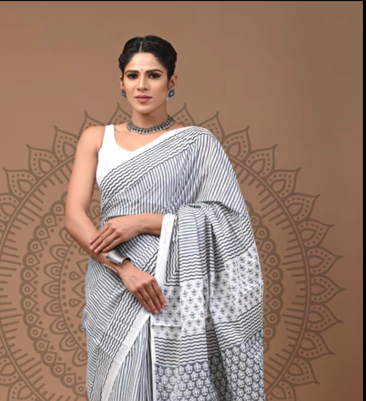 Woman wearing a white saree with black patterns on a brown background