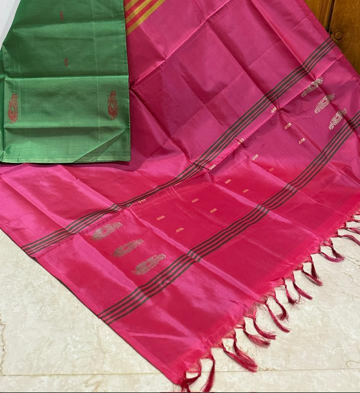 A pink and green silk saree with gold zari stripes, draped to show the pallu and border details against a wooden door background.