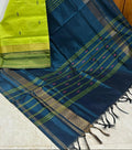 A dark teal blue and lime green saree with gold and silver zari stripes, draped diagonally on a light tiled floor in front of a wooden door.