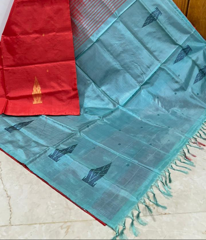 A red and teal blue saree with gold zari patterns, draped to show its border and pallu, set against a wooden door background with the number 983 printed on the right.
