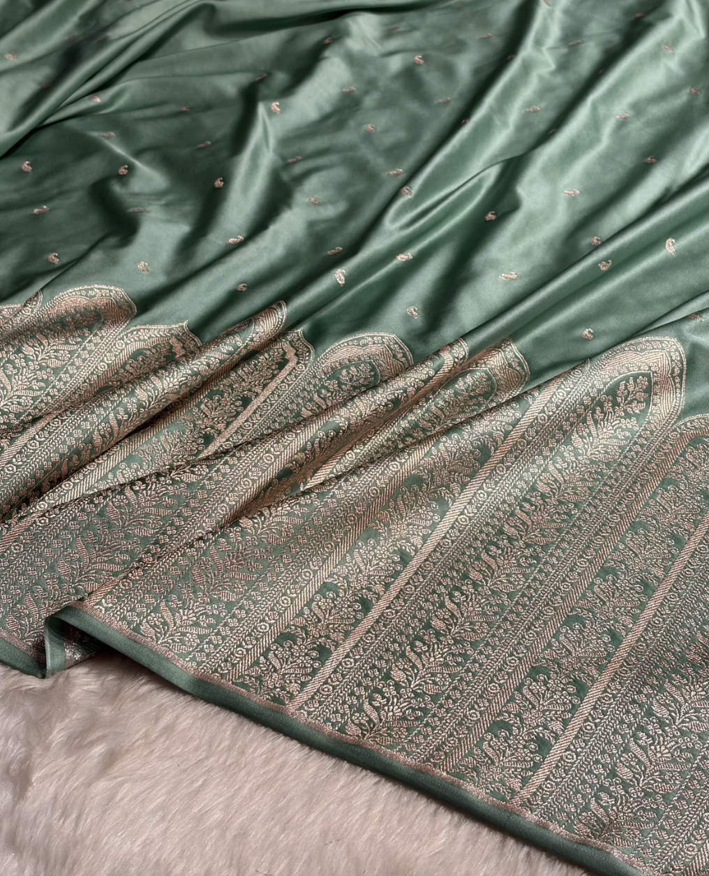 Green fabric with intricate patterns and embroidery, folded on a textured surface.