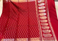 A red silk saree with intricate gold zari weaving, featuring a chevron pattern on the body and a decorative border with paisley motifs.