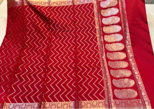 A red silk saree with intricate gold zari weaving, featuring a chevron pattern on the body and a decorative border with paisley motifs.