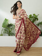 Woman wearing a traditional saree with a red and beige pattern, standing against a white wall with plants.