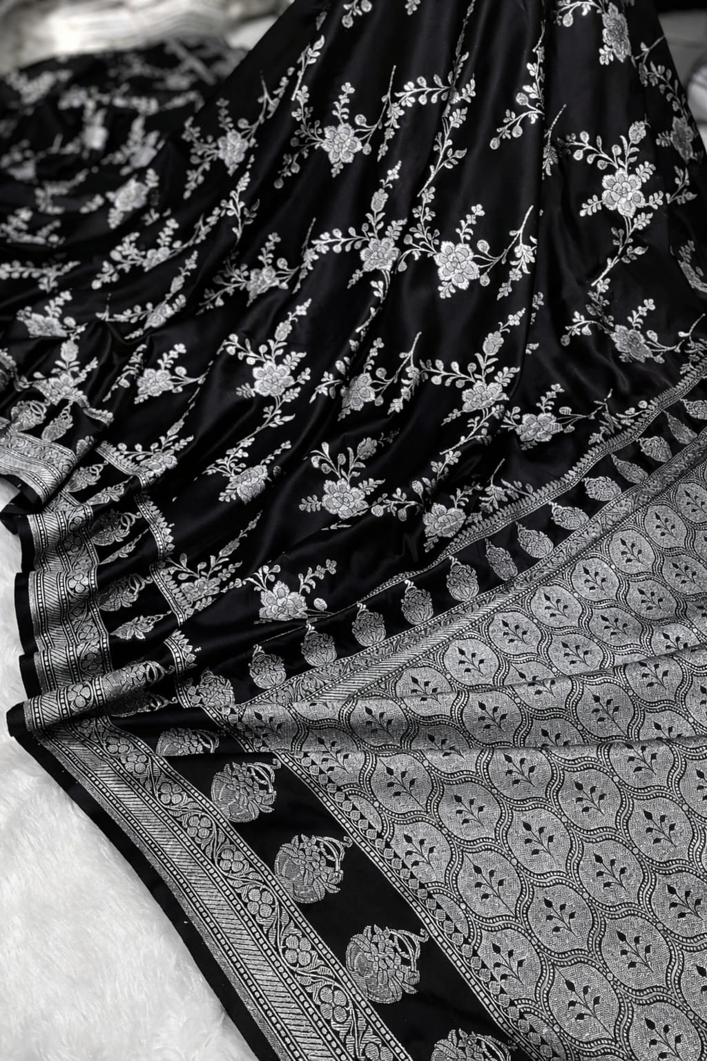 Black saree with white floral patterns and intricate border on a white background