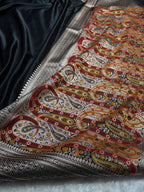 Close-up of a fabric with intricate paisley patterns in red, gold, and black on a dark background.