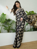 Woman wearing a black saree with elephant patterns in a room with plants.