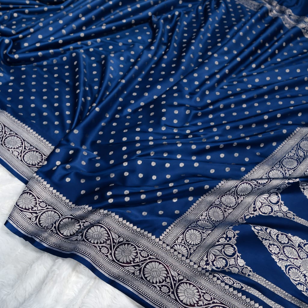 Blue saree with white polka dots and intricate silver border on a white background