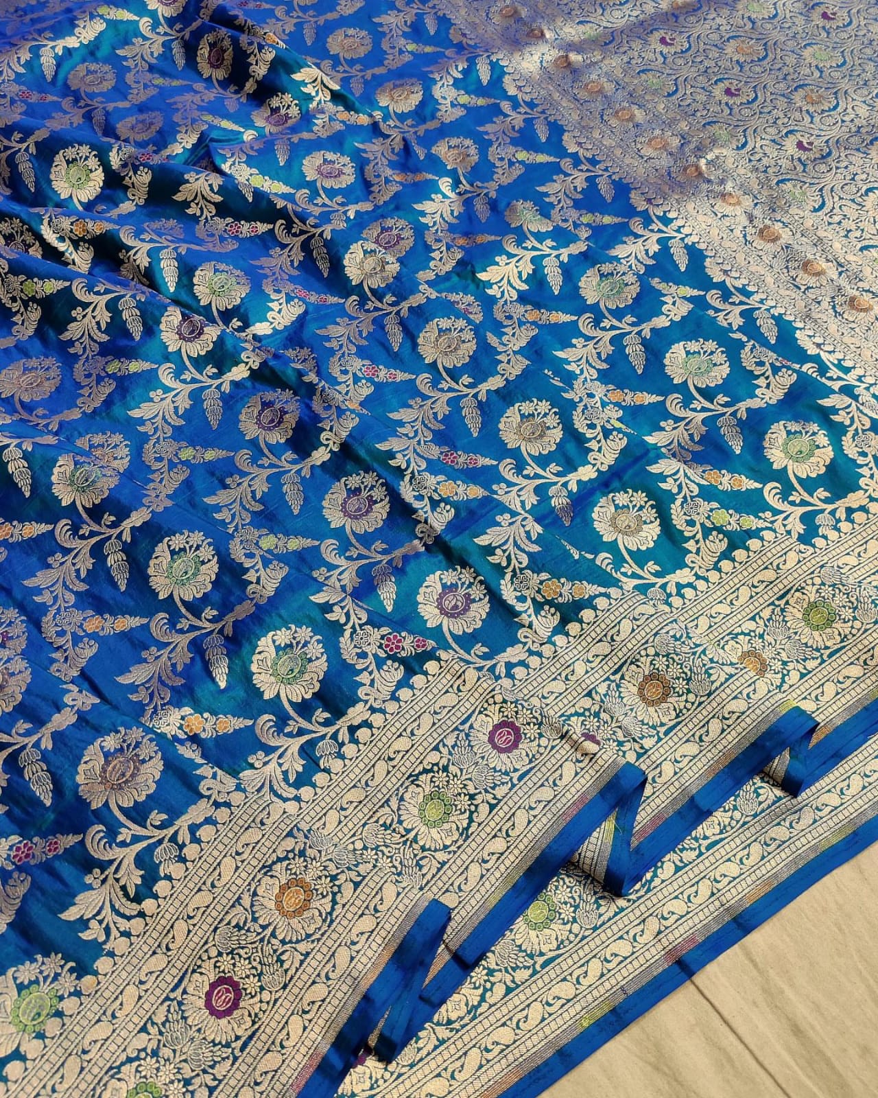 Close-up of a blue fabric with intricate white floral patterns on a wooden surface.