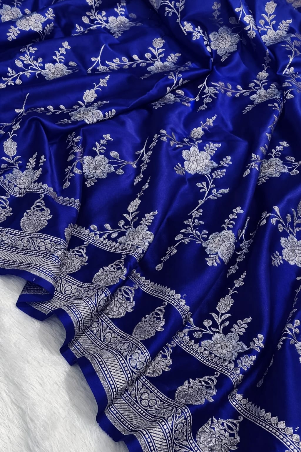 Blue fabric with intricate white floral and leaf patterns on a white background
