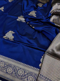 A royal blue silk saree with silver floral motifs and a detailed silver border, draped to show its texture and pattern.