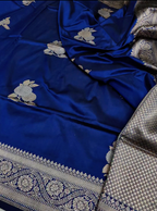 A royal blue silk saree with silver floral motifs and a detailed silver border, draped to show its texture and pattern.