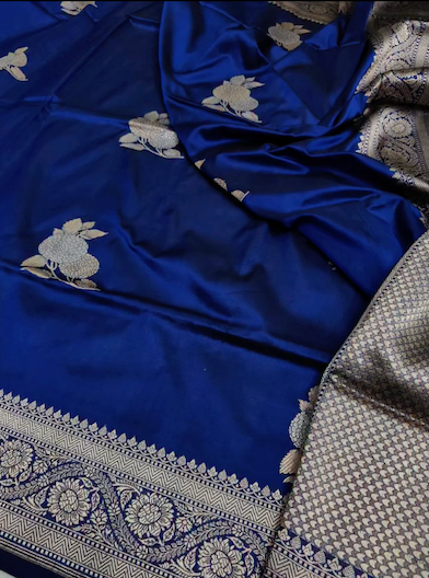 A royal blue silk saree with silver floral motifs and a detailed silver border, draped to show its texture and pattern.