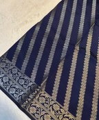 A close-up of a navy blue fabric with vertical metallic gold stripes and an ornate gold border pattern, laid flat on a light textured surface.
