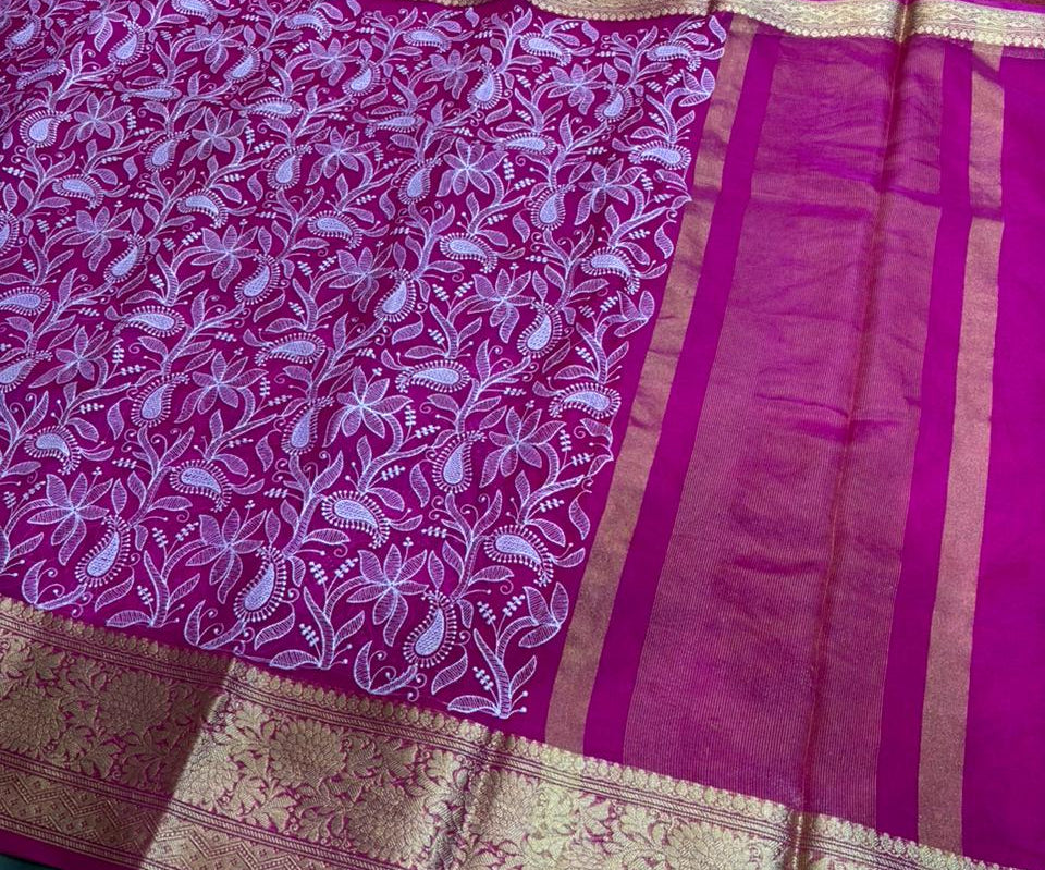 Pink saree with white floral patterns and gold border on a green and red checkered background