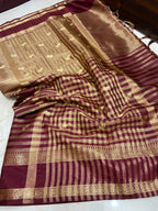 A draped silk saree with a deep maroon body, featuring a gold checkered pattern, a wide gold striped border, and a metallic gold pallu.