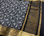 Black saree with white floral patterns and gold border on a red surface
