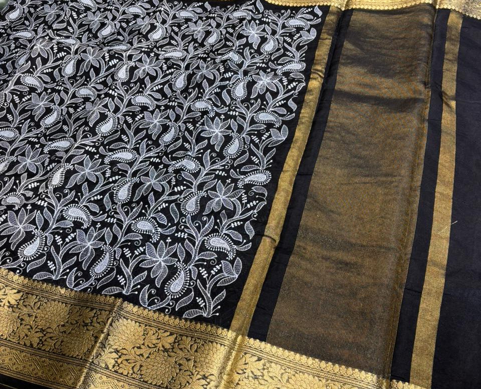 Black saree with white floral patterns and gold border on a red surface