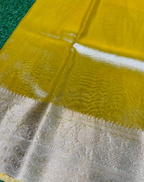 A close-up of a yellow fabric, likely a silk saree or dupatta, featuring a wide beige and gold brocade border with intricate floral patterns.