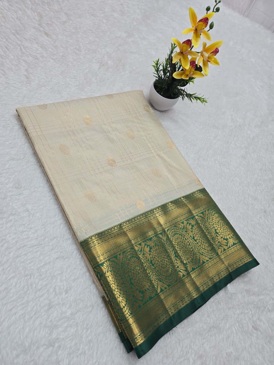 Traditional saree with a green border on a white surface with flowers.