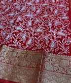 Red saree with white floral patterns and gold border on a green surface