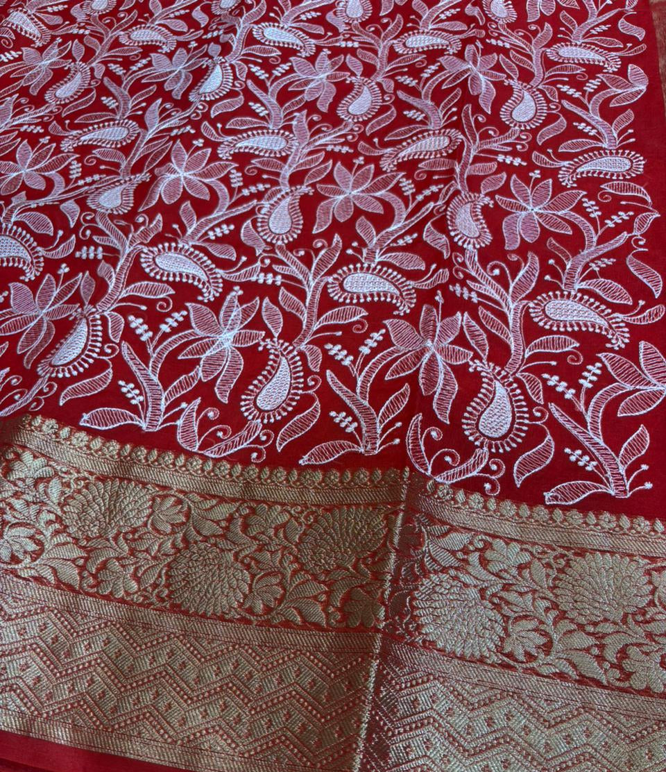 Red saree with white floral patterns and gold border on a green surface