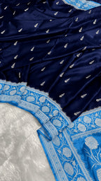 A close-up of a navy blue fabric with small silver motifs and a contrasting light blue border featuring intricate white floral embroidery.