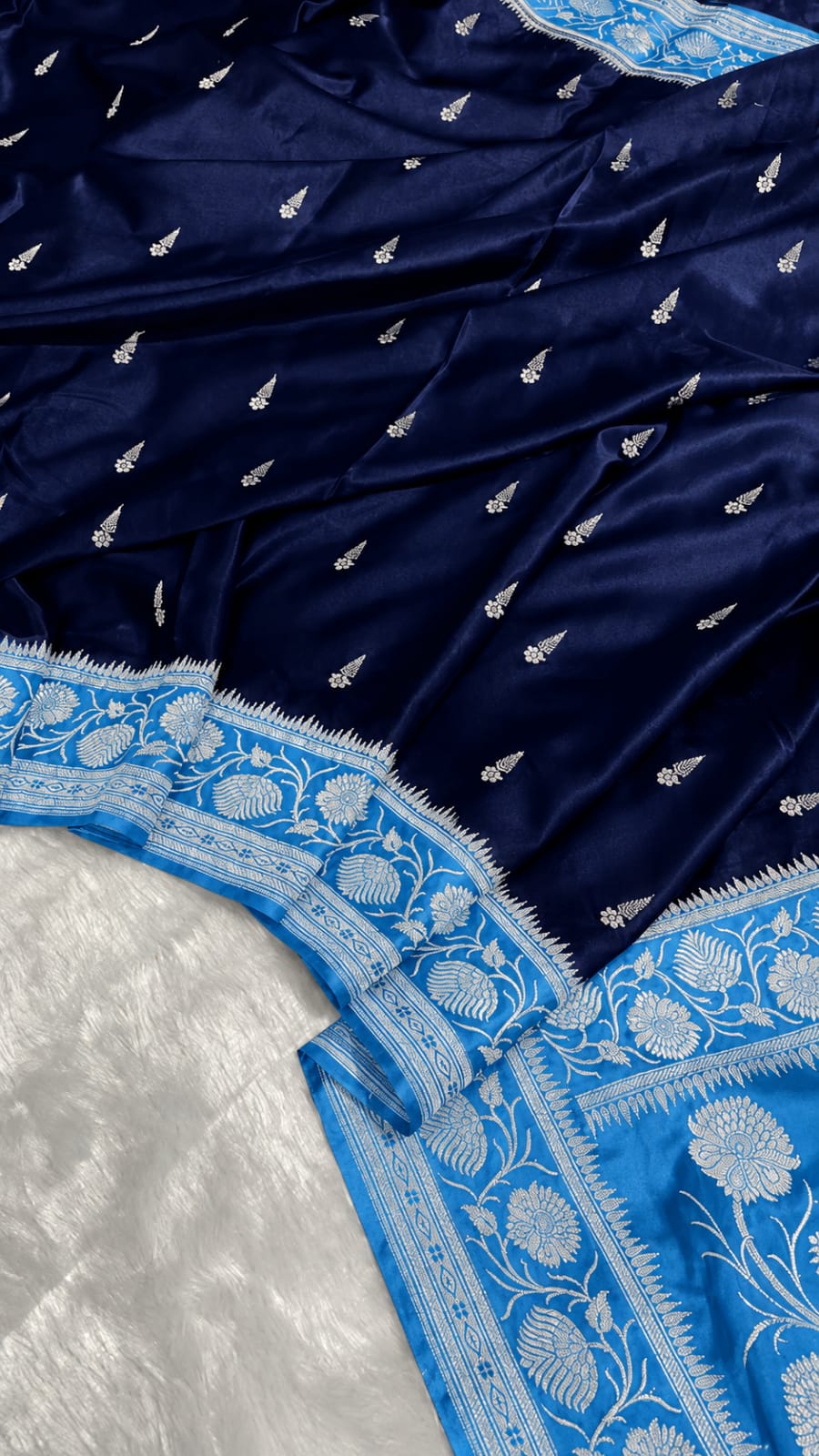 A close-up of a navy blue fabric with small silver motifs and a contrasting light blue border featuring intricate white floral embroidery.
