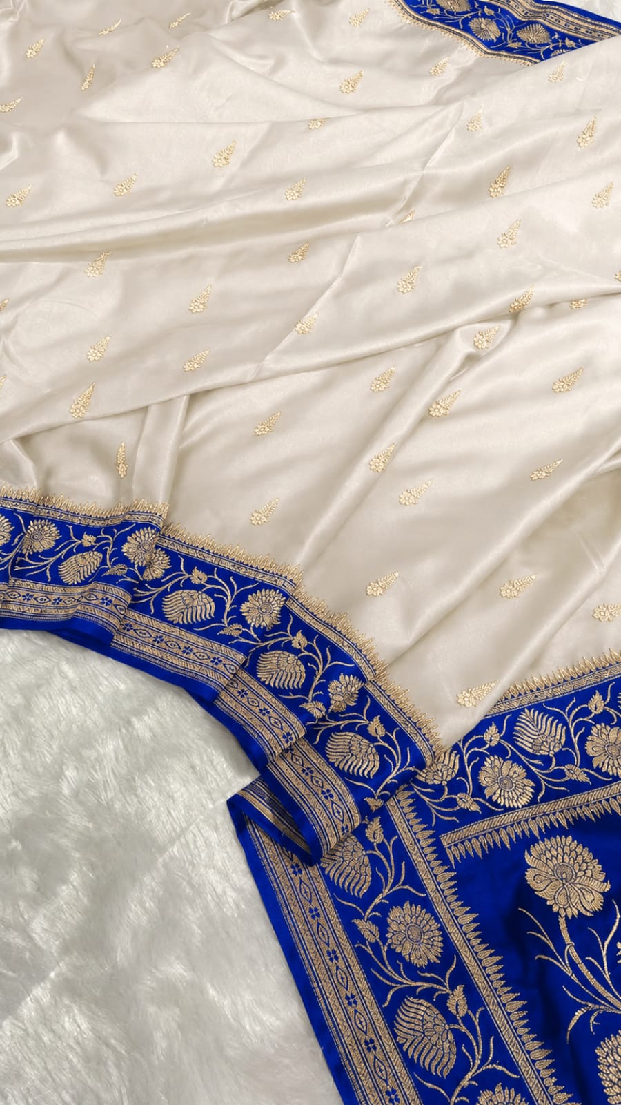 An off-white silk saree with a vibrant royal blue border featuring intricate gold zari embroidery and floral motifs.