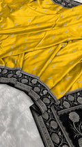A close-up of a yellow silk saree with small silver motifs and a wide black border featuring intricate silver floral embroidery.