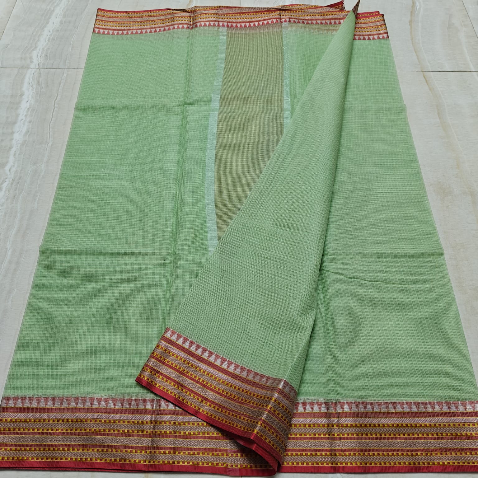 Green saree with a patterned border on a light gray background