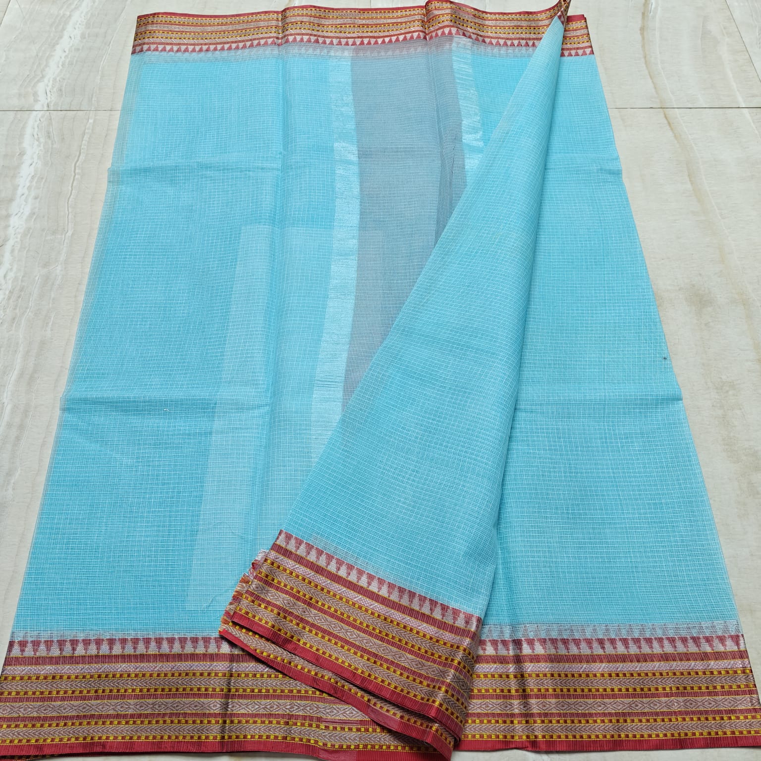 Light blue saree with a patterned border on a light wooden floor.