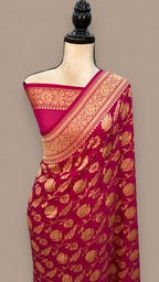 A magenta pink silk saree with intricate gold zari floral brocade work, draped on a cream-colored mannequin torso against a solid taupe background.