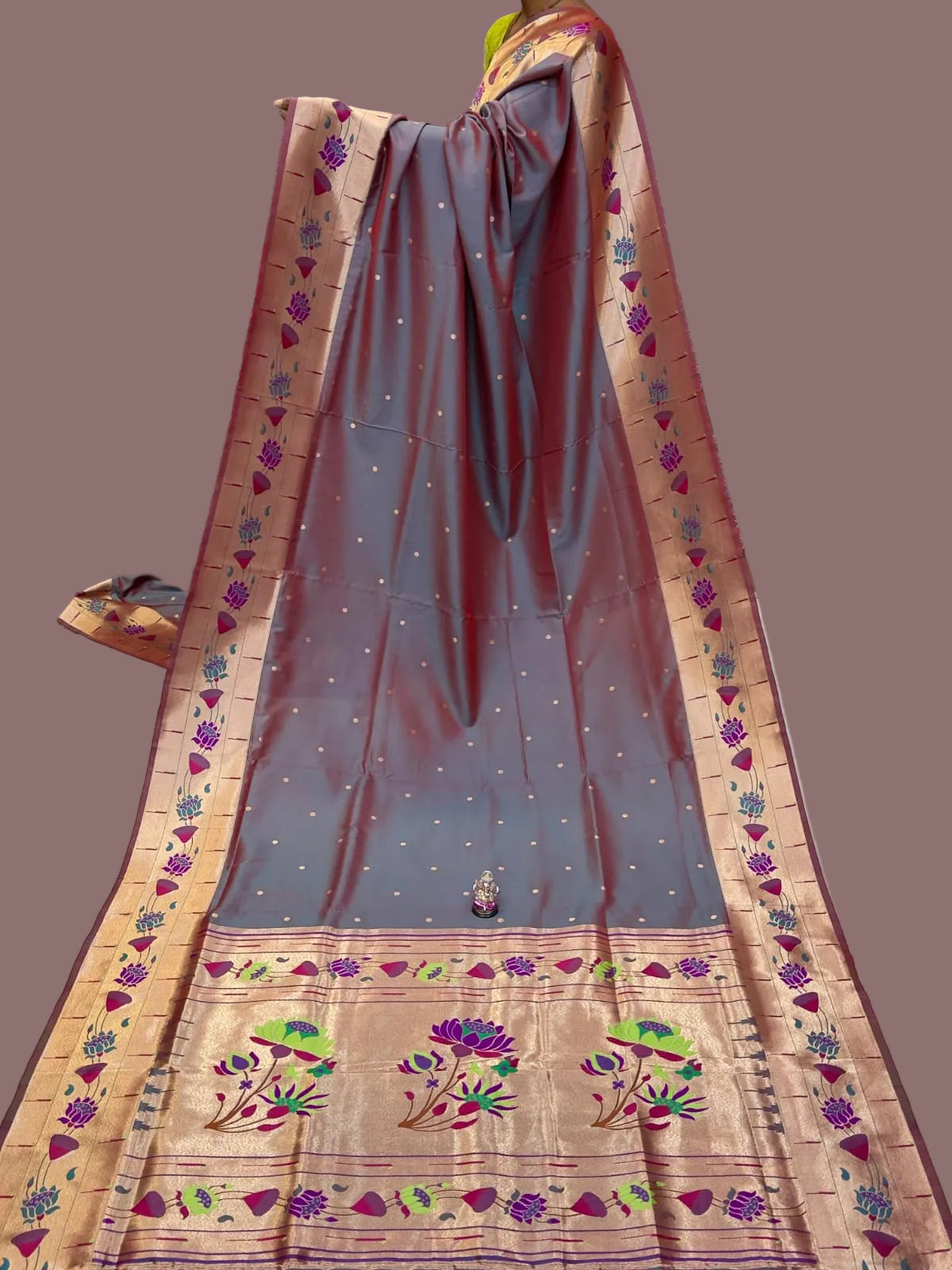 Traditional saree with intricate patterns on a table with stacks of fabric in the background