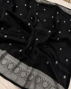 A black silk saree with silver zari embroidery, featuring small dot motifs scattered across the body and a wide decorative border with circular patterns.