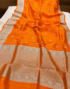 An orange silk saree with intricate white Banarasi zari embroidery, draped to display its border and body pattern.