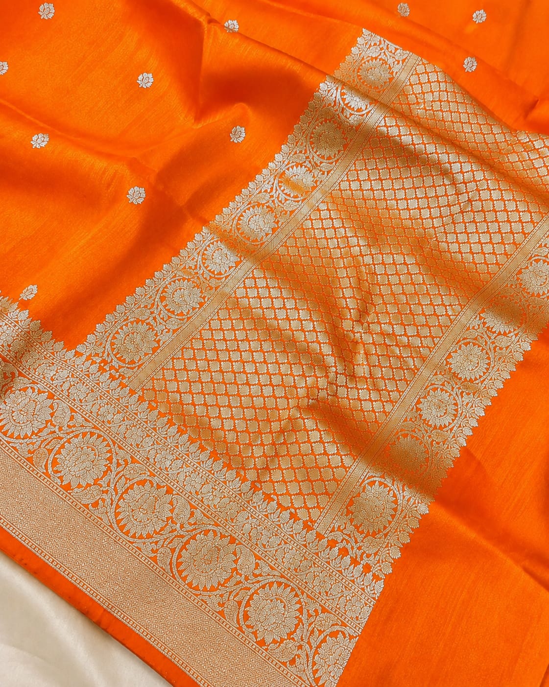 Bright orange Banarasi silk saree with intricate silver zari woven borders and small floral motifs.