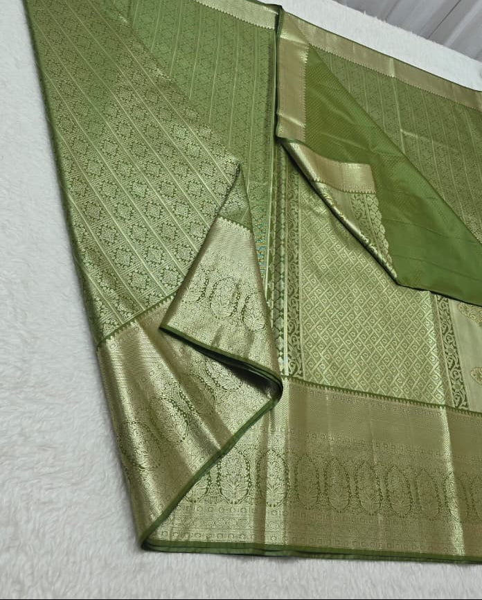 Green saree with intricate patterns on a white surface with flowers in the background