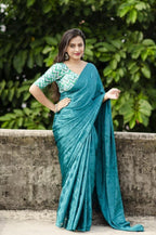 Woman in a teal saree with a green and white blouse against a green leafy background