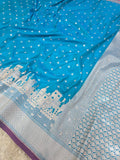 A blue and silver Banarasi silk saree with white zari embroidery, featuring a cityscape motif on the border and a geometric pattern on the pallu.