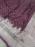 A close-up of a purple fabric, likely a saree, featuring a silver-toned border with architectural motifs and a scattered pattern of small bird silhouettes.
