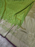 A close-up of a green silk saree with intricate gold zari embroidery, featuring a border with traditional motifs and a dark purple edge.