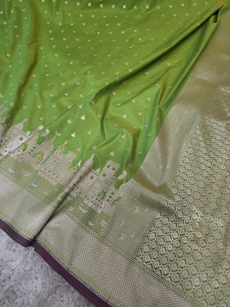 A close-up of a green silk saree with intricate gold zari embroidery, featuring a border with traditional motifs and a dark purple edge.