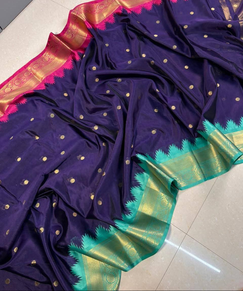 A dark purple silk saree with gold zari motifs, a vibrant pink border, and a green and gold zari pallu, draped on a light gray tiled floor.