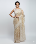 Woman wearing a beige saree with white patterns on a white background