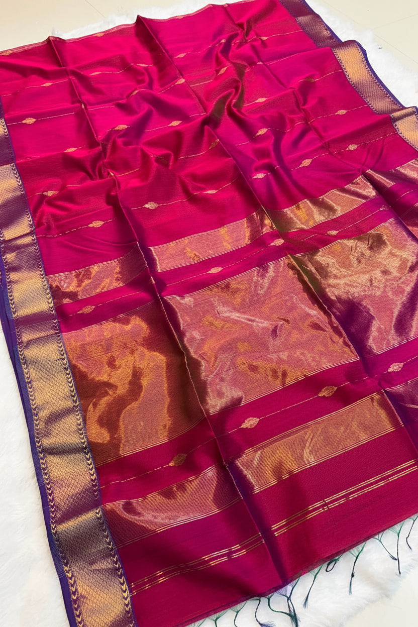 A rich magenta pink silk saree with metallic gold zari borders and motifs, displayed flat with a decorative basket of flowers on a white surface.