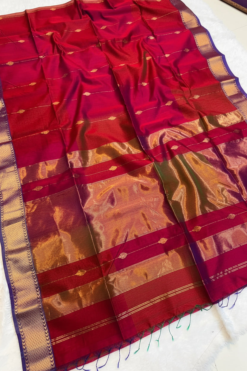 A red and purple silk saree with gold zari metallic borders and motifs, draped flat with a small decorative basket of flowers on top.