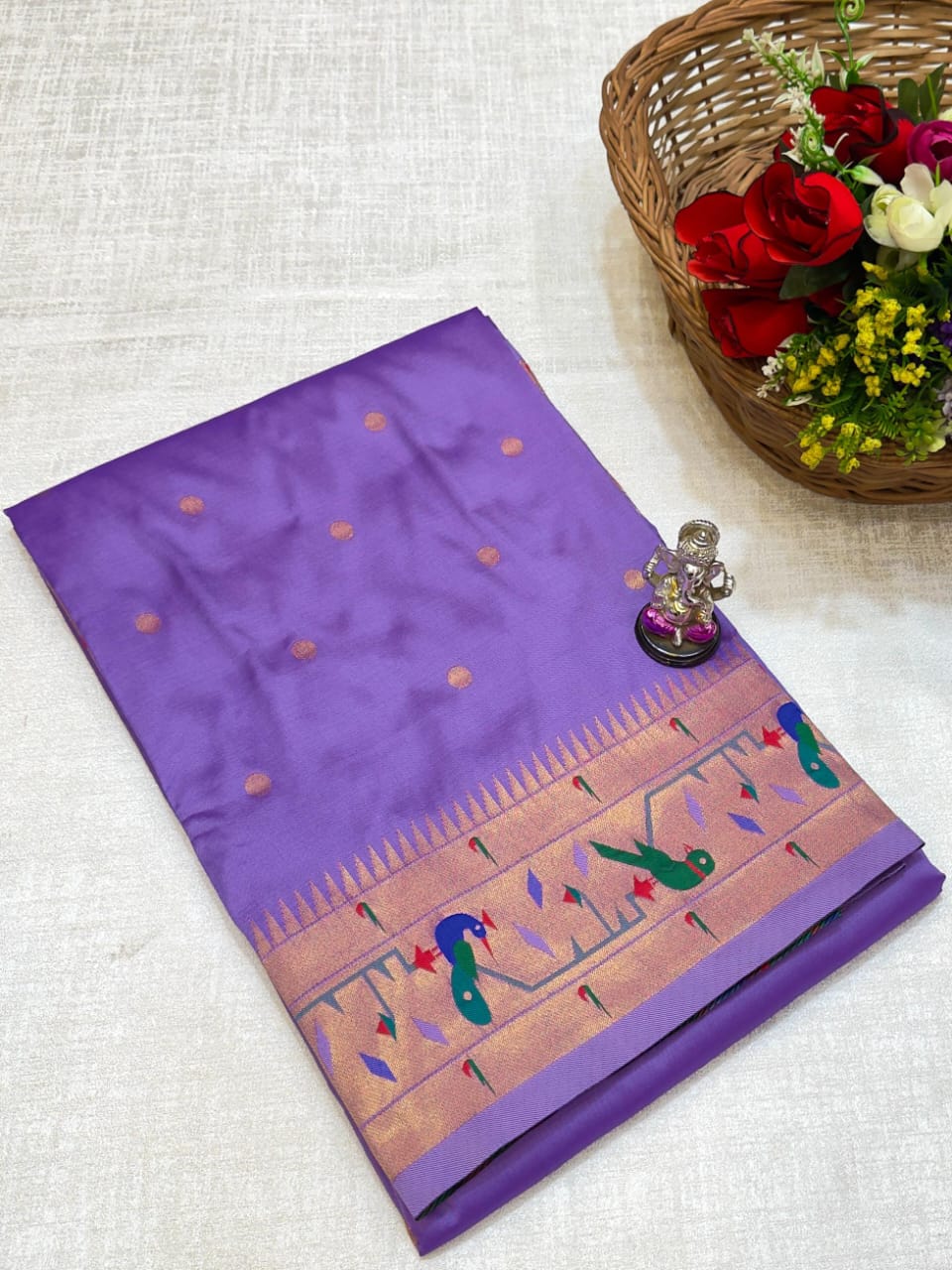 Purple saree with intricate design on a white surface, accompanied by a basket of flowers.