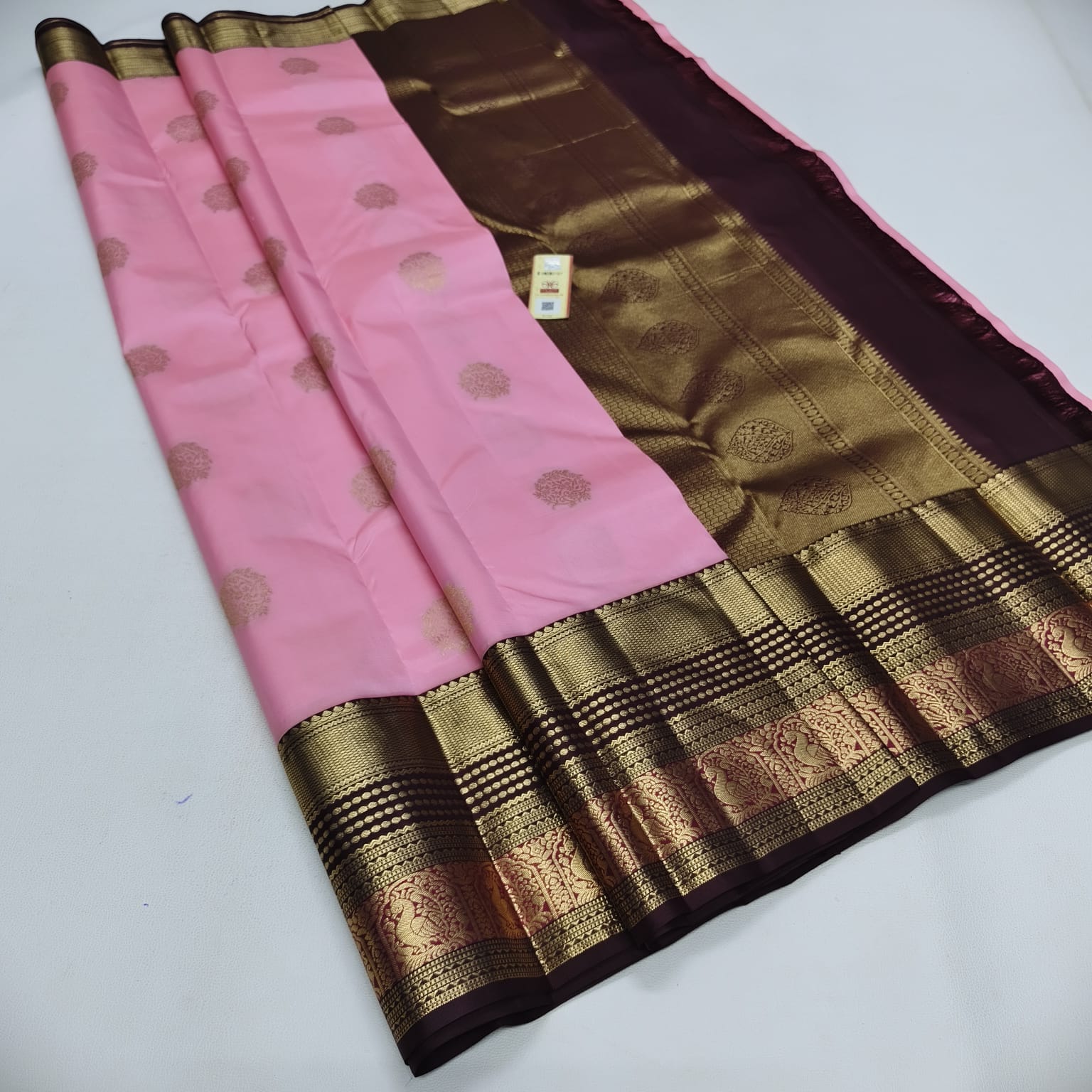 A pink and dark purple Banarasi silk saree with intricate gold zari woven patterns and a wide pleated border, laid out on a white surface.